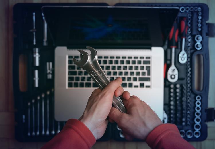 Hands holding two wrenches above a laptop, representing software tools